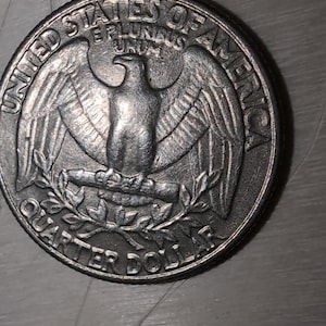 Op de afbeelding: Een close-up van een Amerikaanse kwart dollar munt. De munt toont een adelaar met uitgespreide vleugels, een lauriertak en de woorden "United States of America" en "Quarter Dollar".