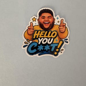 May include: A die-cut sticker featuring a cartoon illustration of a smiling person with a beard wearing a yellow long-sleeve shirt, pointing both index fingers forward. The text reads HELLO YOU C**T! in bold yellow and blue comic-style lettering.
