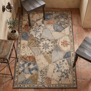 Könnte beinhalten: Ein rechteckiger Teppich mit einem Mosaikmuster aus unregelmäßigen, steinartigen Formen in Blau-, Terrakotta-, Beige- und Cremetönen. Das Design umfasst florale Motive, geometrische Muster und eine dekorative Bordüre mit Dreiecken.