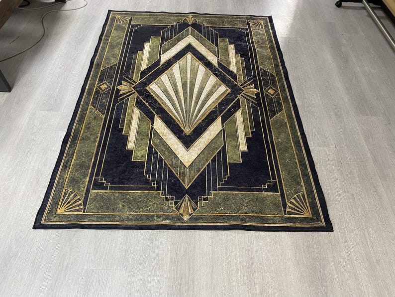 May include: A rectangular area rug featuring a dark navy blue and olive green geometric pattern. The design includes a central diamond shape with radiating fan-like lines, surrounded by layered angular borders and gold-toned accents throughout.