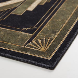 May include: A rectangular mat featuring a dark black and olive green marble-textured surface with gold-toned geometric lines and fan-shaped corner accents. The edges are finished with a black stitched border, creating a structured, linear pattern.