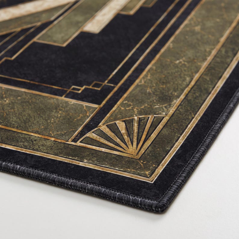 May include: A rectangular mat featuring a dark black and olive green marble-textured surface with gold-toned geometric lines and fan-shaped corner accents. The edges are finished with a black stitched border, creating a structured, linear pattern.