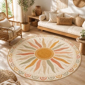 May include: A round area rug featuring a central sun motif with radiating rays in shades of mustard yellow, terracotta, and sage green. The design includes a decorative border with repeating semi-circular patterns and delicate leaf accents.