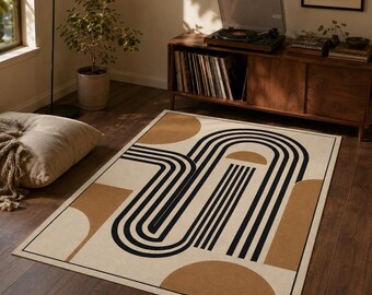 Puede incluir: Una alfombra rectangular con fondo color crema y un patrón geométrico de líneas negras gruesas que forman arcos concéntricos y formas redondeadas, acentuado por semicírculos y bloques rectangulares de color marrón claro.