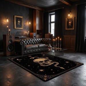 Könnte beinhalten: Ein rechteckiger Teppich mit schwarzem Hintergrund und einem großen, zentralen beigen Totenkopf, der von einer Schlange umschlungen ist. Das Design zeigt Himmelsmotive wie Sterne und Mondsicheln sowie eine verzierte Bordüre im Goldlinien-Stil.