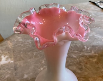 May include: A white and pink glass vase with a ruffled top. The vase has a clear, iridescent finish.