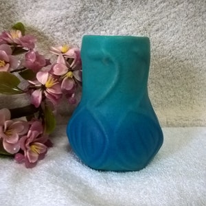 May include: A blue and green ceramic vase with a textured surface and a floral design. The vase is sitting on a white towel.
