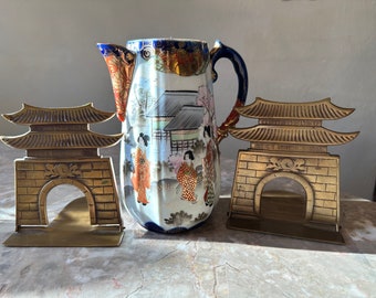 May include: Two gold-colored brass bookends shaped like Japanese pagodas with a white and blue porcelain pitcher with a Japanese scene painted on it.