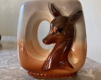 May include: A ceramic vase with a brown and white glaze features a deer head design. The vase has a cutout in the shape of a deer's head.