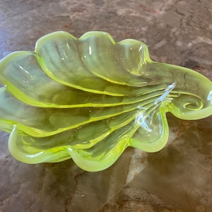 May include: A yellow glass dish shaped like a seashell. The dish has a smooth, glossy finish and is perfect for serving snacks or holding jewelry.
