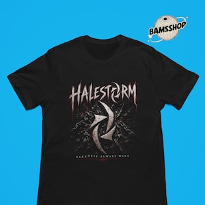 May include: A black short-sleeve t-shirt featuring a graphic print with the band name HALESTORM in a stylized white font, a central metallic-looking emblem, and the text DARKNESS ALWAYS WINS. A small BAMSSHOP logo is visible in the upper right corner.