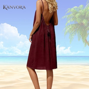 May include: A burgundy-colored, open-back dress with spaghetti straps. The dress is knee-length and has a loose, flowing design. The brand name "KANVORA" is visible in the upper left corner. The background shows a beach scene with a palm tree and blue sky.