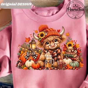 Op de afbeelding: Een roze sweatshirt met een afbeelding van een pluizige hooglandkoe met een oranje gebreide muts, een bril en een geruite sjaal. De koe houdt een mok met slagroom vast. Omringd door pompoenen, herfstbladeren, boeken en een lantaarn.