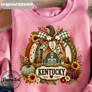 Op de afbeelding: Een lichtroze sweatshirt met een afbeelding van een grote pompoen versierd met een groen-witte geruite strik, een schuur, zonnebloemen en de tekst "home sweet home" en "KENTUCKY" met een hartje onder de naam van de staat.
