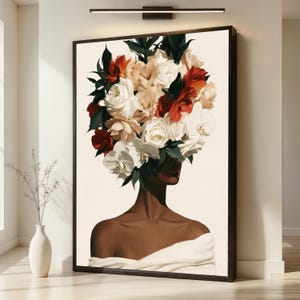 Puede incluir: Una impresión de arte mural enmarcada que representa a una persona de piel oscura con los hombros cubiertos por una tela blanca. La cabeza está reemplazada por un denso arreglo de rosas y orquídeas blancas, crema y rojo oscuro sobre fondo crema.