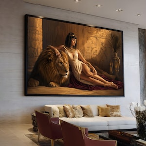 May include: A large framed artwork depicts a woman in a white dress reclining with a lion. The artwork has a gold and brown color scheme, with Egyptian-inspired hieroglyphs in the background. The woman wears gold jewelry.