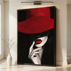 Puede incluir: Una impresión de arte enmarcada que presenta un retrato de alto contraste de un rostro parcialmente oculto por un sombrero rojo de ala ancha. La imagen utiliza una paleta en blanco y negro con acentos de color rojo vibrante en el sombrero y labios.