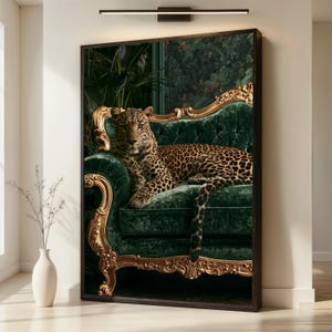 Puede incluir: Una impresión de arte mural enmarcada que muestra un leopardo descansando sobre un sofá de terciopelo verde esmeralda capitoné con un marco de madera tallada en oro. El fondo muestra follaje verde oscuro en una pared clara.