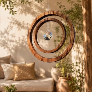 May include: A hanging ornament featuring two concentric dark brown wooden rings suspended by a thin silver wire. A clear, multifaceted crystal sphere hangs from a silver beaded chain in the center of the rings, catching and reflecting light.