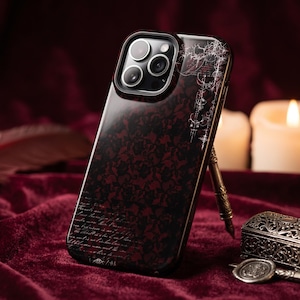 Puede incluir: Una funda para smartphone con un patrón de encaje floral en rojo oscuro y negro, detalles de líneas blancas en la esquina superior derecha y texto en cursiva en la parte inferior. La funda tiene un recorte para un sistema de triple cámara.
