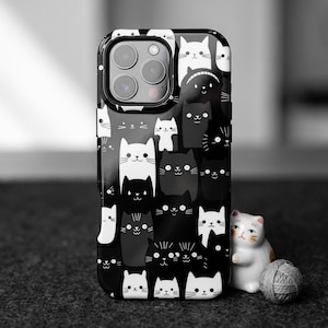Puede incluir: Una funda de smartphone negra con un patrón repetitivo de caras de gato estilizadas en blanco y negro con rasgos dibujados con líneas simples. El diseño cubre toda la parte posterior de la funda, incluyendo el área alrededor de la cámara.