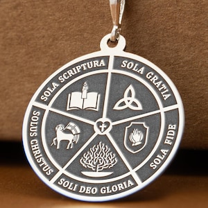 Puede incluir: Collar con colgante de plata con un dije circular con símbolos religiosos y texto grabados. El dije está suspendido de una delicada cadena. El texto incluye "SOLA SCRIPTURA", "SOLA GRATIA", "SOLA FIDE", "SOLI DEO GLORIA" y "SOLUS CHRISTUS".