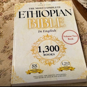May include: The Most Complete Ethiopian Bible, Volume Two, in English. The book cover is cream-colored with gold accents and text. It features the text "1,300 BOOKS" in a gold circle, and includes the missing Apocrypha.