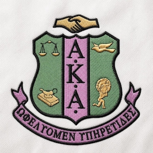 May include: An embroidered crest featuring a green shield with a central pink vertical stripe containing the letters A.K.A. Symbols include a scale, a dove, a lamp on a book, and a figure carrying a globe. A handshake sits above, with a pink banner below.