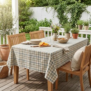 May include: A rectangular dining table with a light blue and white checkered tablecloth featuring a subtle botanical print. The table is set with a stack of white plates, a wooden cutting board with orange slices, and a ceramic bowl of food.