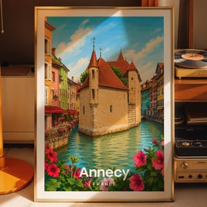 Può includere: Stampa artistica incorniciata raffigurante Annecy, Francia. L'opera d'arte mostra un canale con edifici, un castello e fiori vibranti. Il testo "Annecy FRANCE" è visualizzato in basso.