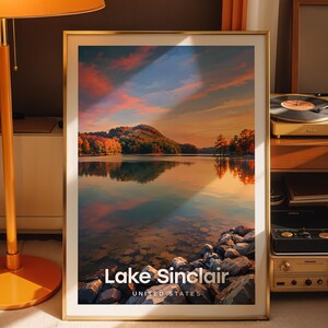 Könnte beinhalten: Ein gerahmter vertikaler Wandkunstdruck mit einer Landschaft des Lake Sinclair, Vereinigte Staaten. Das Bild zeigt einen ruhigen See, der einen Sonnenuntergangshimmel mit orangefarbenen und blauen Wolken reflektiert, umgeben von Bäumen und einem felsigen Ufer.