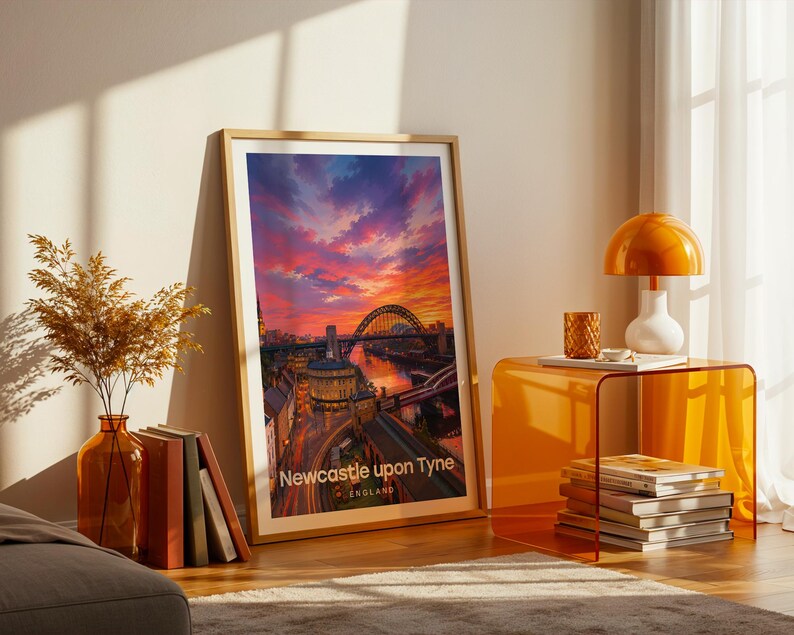 A vibrant Newcastle upon Tyne artwork rendered in high-detail illustrative style, placing the Tyne Bridge at the heart of the composition with Grey Street's Georgian sweep and Grey's Monument rising above the River Tyne in warm layered tones. Bold white NEWCASTLE UPON TYNE typography sits beneath drifting illustrated clouds. Gold frame leaning against a cream wall on parquet flooring, paired with an amber glass vase, stacked books, and an amber side table with an orange dome lamp.
