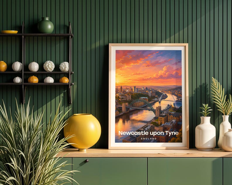 This contemporary Newcastle upon Tyne print celebrates the city's iconic riverscape — the Tyne Bridge and Millennium Bridge spanning the Tyne above the stacked quayside buildings, rendered with bold white NEWCASTLE typography and an open illustrated sky. Oak frame displayed against a deep green panelled wall alongside an oak console, black metal shelving, a yellow globe vase, white ceramic vessels, and layered botanicals.