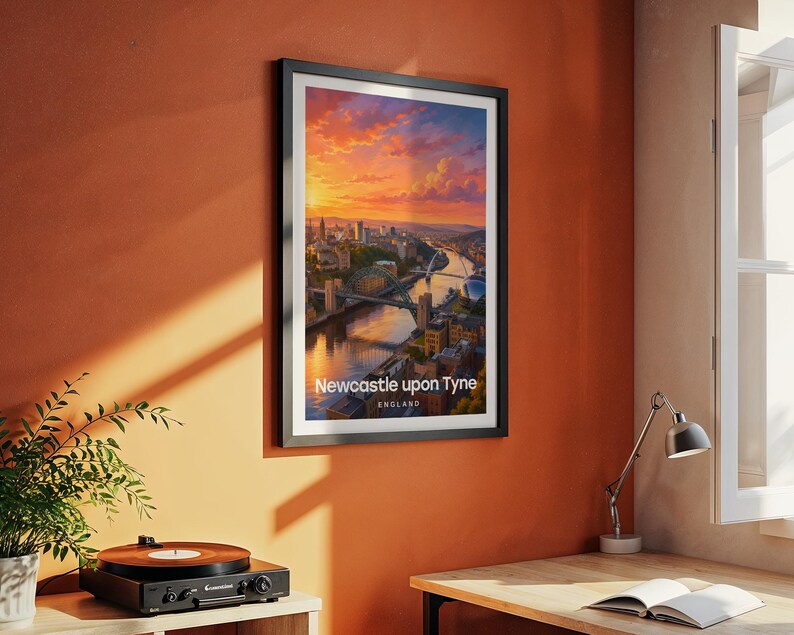 Modern Newcastle city art bringing the Tyne Bridge, Millennium Bridge, and the warm-toned Victorian quayside of the River Tyne to life in rich illustrative colour with bold white NEWCASTLE typography against a luminous illustrated sky. Black frame hung on a textured terracotta wall in a room styled with a vintage record player, yellow desk lamp, open book, green plant, and an angled metal work lamp.