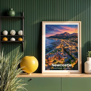This contemporary Newcastle print celebrates the sandy promenade beach, the mighty peak of Slieve Donard climbing straight from the shore, and the rolling Mourne Mountains framing the seaside town in rich warm tones. Bold white NEWCASTLE typography sits beneath an open sky of drifting clouds and circling birds. Framed in light oak against a dark green shiplap wall with a black metal shelving unit and yellow globe vase.