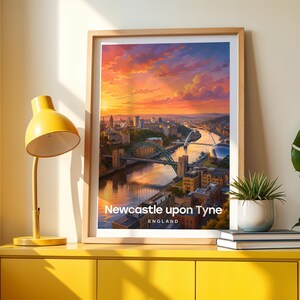Framed Newcastle upon Tyne wall art print featuring the Tyne Bridge arching over the River Tyne, with the Millennium Bridge and the layered Victorian quayside buildings of the Gateshead bank beyond. High-detail illustrated cityscape with rich warm colour, bold white NEWCASTLE typography, and an open illustrated sky with drifting clouds. Oak frame leaning against a cream wall beside a yellow console, stacked books, and a green plant in a white pot, warm window light casting soft shadow patterns.