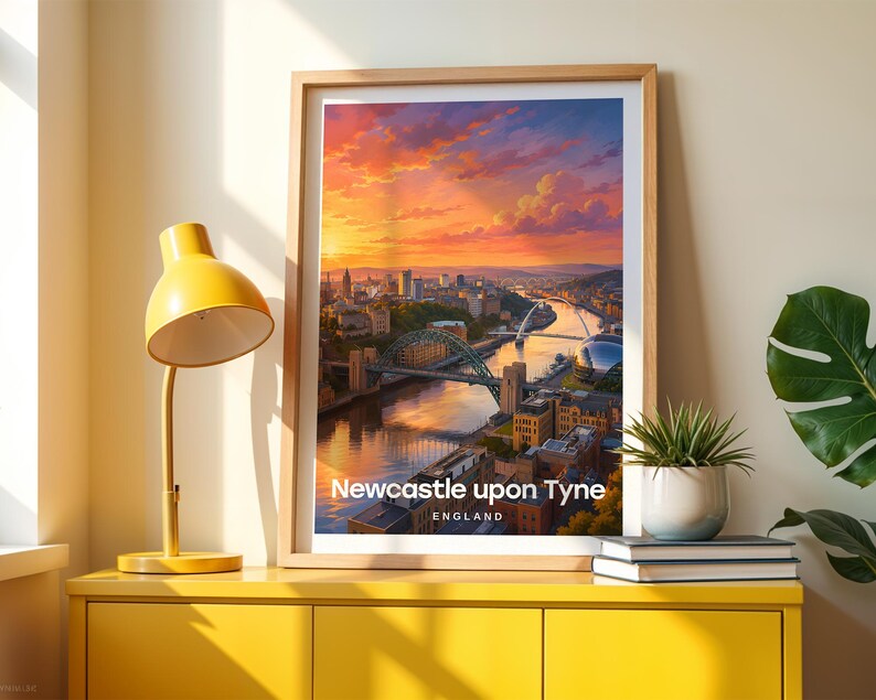Framed Newcastle upon Tyne wall art print featuring the Tyne Bridge arching over the River Tyne, with the Millennium Bridge and the layered Victorian quayside buildings of the Gateshead bank beyond. High-detail illustrated cityscape with rich warm colour, bold white NEWCASTLE typography, and an open illustrated sky with drifting clouds. Oak frame leaning against a cream wall beside a yellow console, stacked books, and a green plant in a white pot, warm window light casting soft shadow patterns.