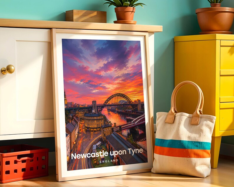 Newcastle upon Tyne poster capturing the Tyne Bridge over the River Tyne with the sweeping Georgian facades of Grey Street and the column of Grey's Monument rising behind, rendered in rich warm illustrative colour. Bold white NEWCASTLE UPON TYNE typography and drifting clouds complete the composition. Oak frame leaning against a teal wall beside a white cabinet, yellow drawer unit, terracotta plant pots, a cloth bag, and a red plastic crate.
