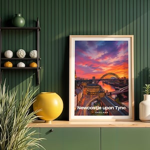 This contemporary Newcastle upon Tyne print celebrates the city's defining view — the Tyne Bridge spanning the river with Grey Street's curved Georgian terraces and Grey's Monument towering on the hill, rendered with bold white NEWCASTLE UPON TYNE typography and an open illustrated sky. Oak frame displayed against a deep green panelled wall alongside an oak console, black metal shelving, a yellow globe vase, white ceramic vessels, and layered botanicals.