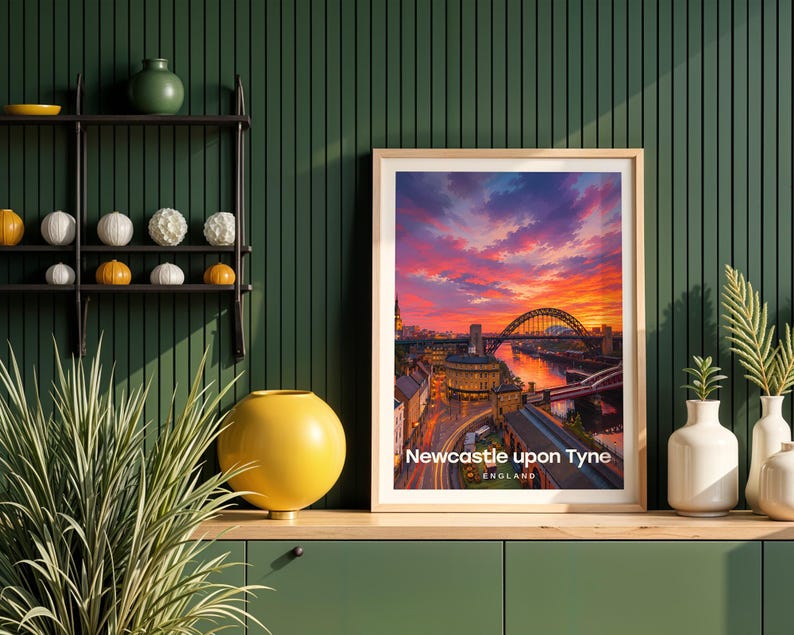 This contemporary Newcastle upon Tyne print celebrates the city's defining view — the Tyne Bridge spanning the river with Grey Street's curved Georgian terraces and Grey's Monument towering on the hill, rendered with bold white NEWCASTLE UPON TYNE typography and an open illustrated sky. Oak frame displayed against a deep green panelled wall alongside an oak console, black metal shelving, a yellow globe vase, white ceramic vessels, and layered botanicals.