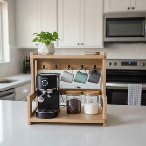 Könnte beinhalten: Ein hölzerner Kaffeebereich mit einer schwarzen Espressomaschine, drei hängenden Tassen und Gläsern mit Kaffeebohnen und Zucker. Eine kleine Pflanze in einem weißen geometrischen Topf steht oben.