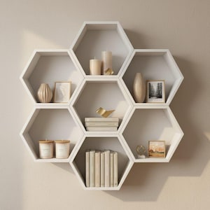 Op de afbeelding: Witte honingraatvormige wandplanken met diverse decoratieve items. De planken bevatten kaarsen, vazen, ingelijste foto's, boeken en een gouden vogelbeeldje. De items zijn geordend voor een stijlvolle presentatie.