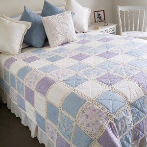 Pu&ograve; includere: Una trapunta patchwork caratterizzata da una griglia di pannelli quadrati in tessuto nelle tonalit&agrave; azzurro, lavanda e bianco, con alcuni quadrati che presentano un motivo floreale. I quadrati sono uniti da un bordo all'uncinetto color crema.