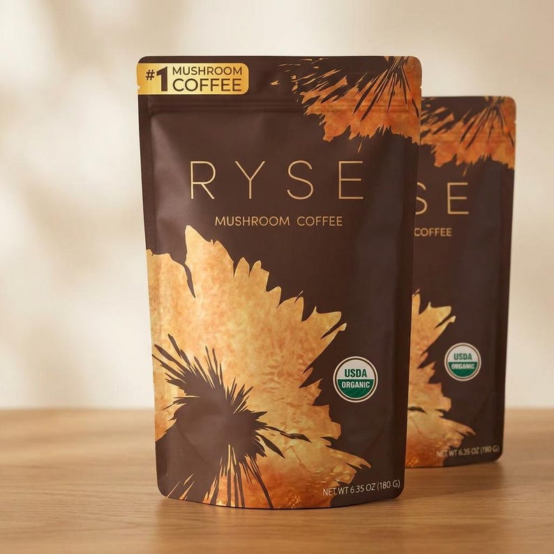 May include: Two brown pouches of RYSE Mushroom Coffee. The front pouch has a large gold floral design and the text "RYSE MUSHROOM COFFEE". The pouches are labeled "USDA ORGANIC" and "NET WT 6.35 OZ (180 G)".