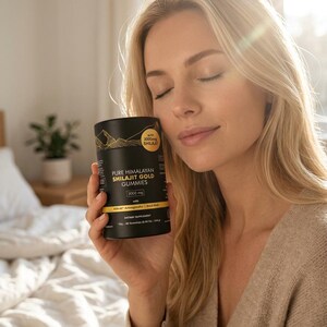 May include: A black cylindrical container of Pure Himalayan Shilajit Gold Gummies is held by a person. The container has gold lettering and a mountain graphic. The text on the container reads "3000 mg" and "Dietary Supplement".