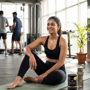 May include: A woman in black athletic wear sits on a green yoga mat in a gym. She wears a black sports bra and leggings. A black and gold container and a water bottle are next to her. The text on the container reads "BE PURE HIMALAYAN SILANT GOLD CRANBERRIES."