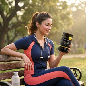 May include: A woman in athletic wear sits on a park bench, holding a black supplement container. The container has gold lettering and a yellow sticker. She wears a navy blue and coral athletic top and leggings. A water bottle sits on the bench.