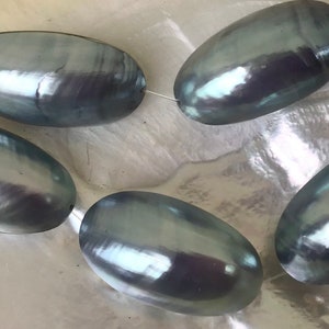 May include: Five oval-shaped, iridescent beads strung together. The beads have a dark gray color with a pearlescent sheen, reflecting light. The beads are strung on a thin, clear string, and are likely used for jewelry making.