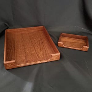 May include: A large rectangular wooden desk tray and a smaller matching rectangular wooden tray, both featuring a rich brown wood grain finish, raised sides, and a U-shaped cutout on the front edge for easy access to contents.
