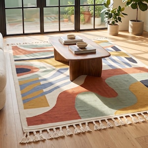 Puede incluir: Una alfombra rectangular con un patr&oacute;n abstracto de formas org&aacute;nicas y l&iacute;neas onduladas en tonos terracota, verde salvia, amarillo mostaza, azul marino y crema. La alfombra est&aacute; rematada con flecos de color crema en ambos extremos cortos.